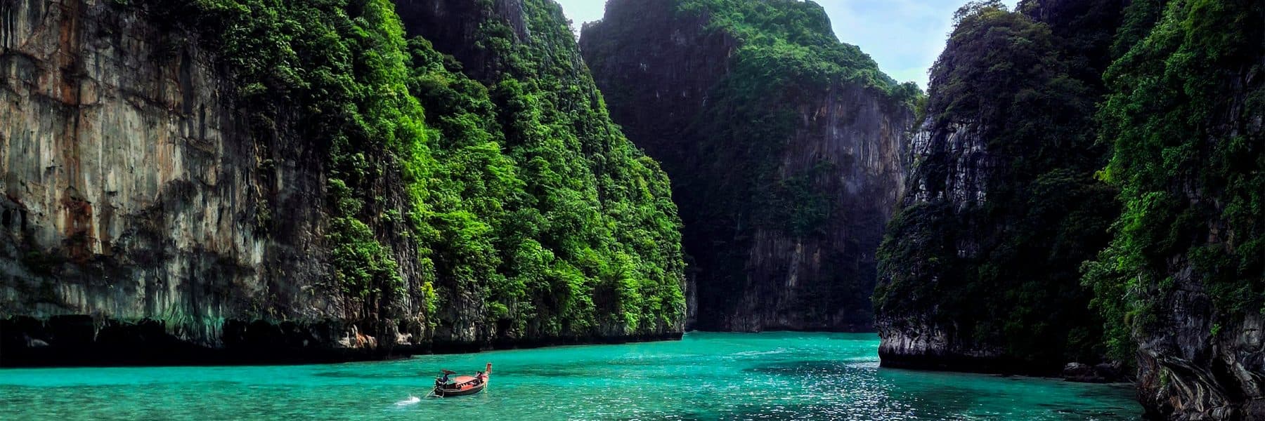 A long-tail boat in a turquoise lagoon between limestone cliffs, Thailand